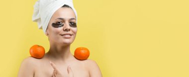 Yüzünde altın besleyici maske olan beyaz havluyla kadın portresi. Cilt temizleme organik kozmetik rahatlama konsepti. Sırtı turuncu bir mandalina tutan bir kız..