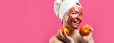 Kafasında kırmızı besleyici maske olan beyaz havluyla güzel bir kadın portresi. Cilt temizleme organik kozmetik rahatlama konsepti. Sırtı turuncu bir mandalina tutan bir kız..