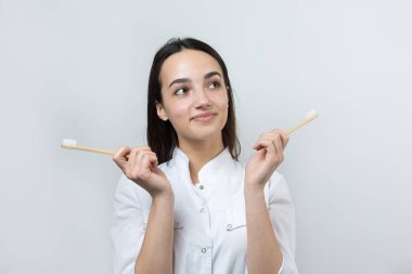 Genç bir esmer kız elinde ekolojik bir diş fırçası tutuyor. Beyaz önlüklü bir kız sıfır israfı teşvik eder..