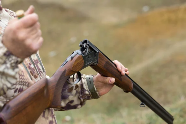 Charges a hunting smooth-bore rifle, hunting a pheasant with dogs. A hunter in camouflage is standing with a weapon.