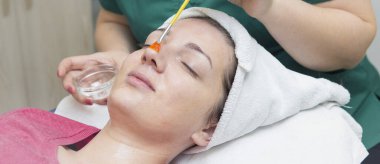 Yüz bakımı. Güzellik uzmanı güzellik salonunda fırça kullanarak yüzüne güzellik maskesi takıyor.