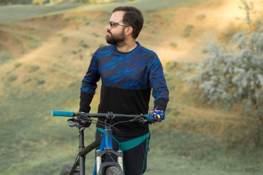 Taze yeşil yaz ormanının arka planına karşı bir uçurumun üzerinde duran bir hava süspansiyon çatal ile modern bir karbon hardtail bisiklet üzerinde şort ve mayo Bisikletçi