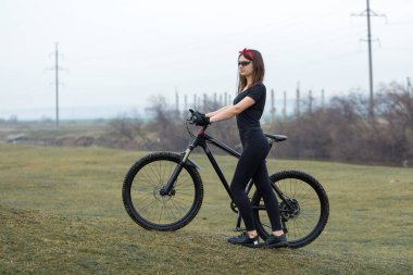 Dağ bisikletli bir kız, yağmurlu havada bisiklet süren bir bisikletçinin güzel portresi spor kıyafetlerinde modern karbon fiber dağ bisikleti süren bir spor kızı. Kırmızı bandanalı bir kızın yakın plan portresi..