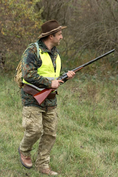 Hunting period, autumn season open. A hunter with a gun in his hands in hunting clothes in the autumn forest in search of a trophy. A man stands with weapons and hunting dogs tracking down the game.