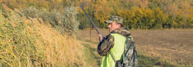 Avcı elinde silahla bozkırın arka planında. Sonbaharda sabahın erken saatlerinde sülün avı. Panoramik resim, tonlanmış.