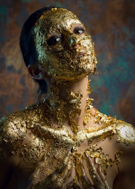Yüzünde altın yapraktan yapılmış bir maske olan bir kız. Soyut bir arka planda esmer bir kadının kasvetli stüdyo portresi.