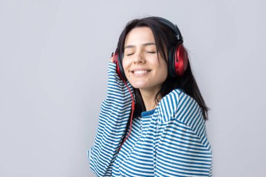 Çizgili yelek giymiş genç bir kız stüdyoda kırmızı kulaklıkla müzik dinliyor ve dans ediyor..