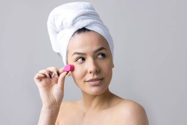 Kafasında beyaz havluyla güzel bir kadın portresi ve pembe bir kalbe bakan bir vücut için sünger. Cilt temizleme eko organik kozmetik rahatlama konsepti.