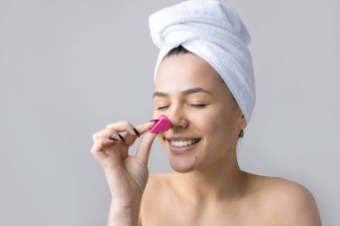 Kafasında beyaz havluyla güzel bir kadın portresi ve pembe bir kalbe bakan bir vücut için sünger. Cilt temizleme eko organik kozmetik rahatlama konsepti.