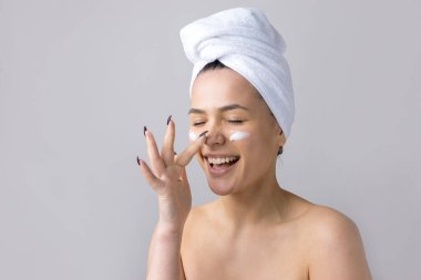 Kafasında beyaz havlu olan bir kadının güzel portresi yüzüne krem sürüyor. Cilt temizleme eko organik kozmetik rahatlama konsepti.