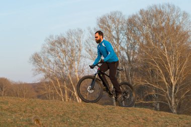 Pantolon ve yün ceketli bir bisikletçi. Havalandırma çatallı, modern bir karbon motorlu. Tepedeki adam bisiklete biniyor..