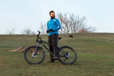 Pantolon ve yün ceketli bir bisikletçi. Havalandırma çatallı, modern bir karbon motorlu. Tepedeki adam bisiklete biniyor..