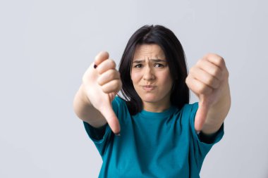 Mavi kolsuz tişörtlü genç bir esmer, olumsuz bir ifadeyle başparmak hareketi yapıyor.