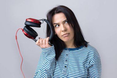 Çizgili yelek giymiş genç bir kız stüdyoda kırmızı kulaklıkla müzik dinliyor ve dans ediyor..