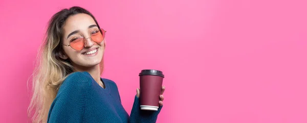 ピンクの背景にコーヒーを飲みながら青いセーターを着たグラマーな女性 — ストック写真