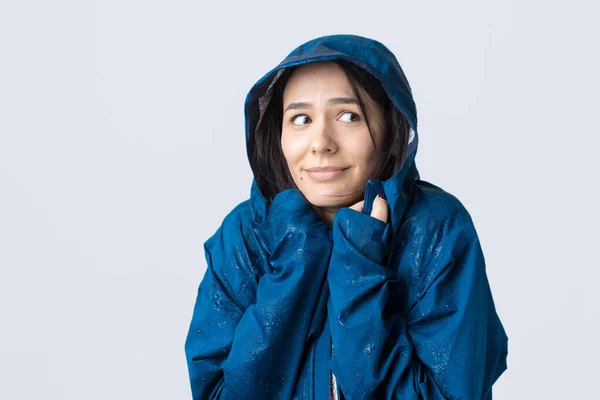 笑顔の女の子の肖像画で青レインコートに身を包んだ滴でフードととともに灰色の背景でスタジオ — ストック写真