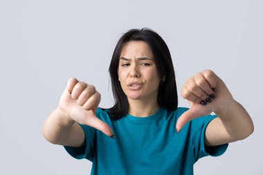 Mavi kolsuz tişörtlü genç bir esmer, olumsuz bir ifadeyle başparmak hareketi yapıyor.