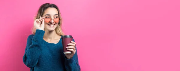 ピンクの背景にコーヒーを飲みながら青いセーターを着たグラマーな女性 — ストック写真