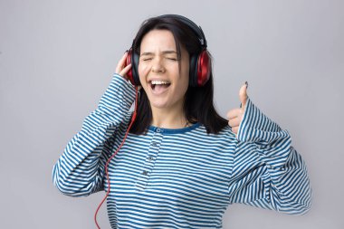 Çizgili yelek giymiş genç bir kız stüdyoda kırmızı kulaklıkla müzik dinliyor ve dans ediyor..