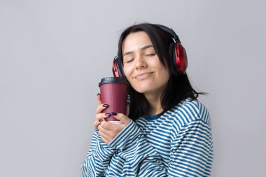 Çizgili yelek giymiş genç bir kız stüdyoda kırmızı kulaklıkla müzik dinliyor ve dans ediyor..