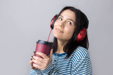 Çizgili yelek giymiş genç bir kız stüdyoda kırmızı kulaklıkla müzik dinliyor ve dans ediyor..