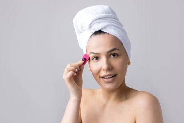 Kafasında beyaz havluyla güzel bir kadın portresi ve pembe bir kalbe bakan bir vücut için sünger. Cilt temizleme eko organik kozmetik rahatlama konsepti.