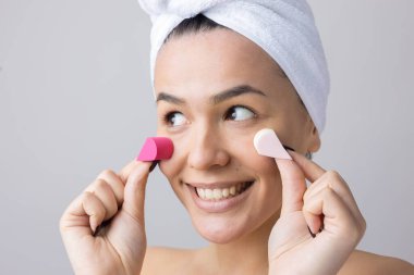 Kafasında beyaz havluyla güzel bir kadın portresi ve pembe bir kalbe bakan bir vücut için sünger. Cilt temizleme eko organik kozmetik rahatlama konsepti.