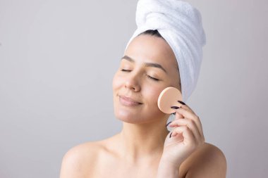 Kafasında beyaz havluyla güzel bir kadın portresi ve pembe bir kalbe bakan bir vücut için sünger. Cilt temizleme eko organik kozmetik rahatlama konsepti.