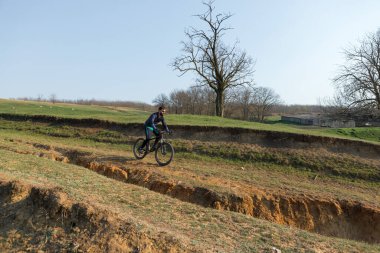 Şortlu ve formalı bisikletçi, modern karbon kuyruklu motorsikletli. Uçurumun kenarında, yeşil bahar ormanlarının arka planında duran bir hava süspansiyon çatalı var.