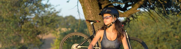 骑越野山地自行车的女孩 日落时骑自行车的美丽画像 穿着运动服骑着现代碳纤维山地自行车的健身女孩 戴头盔和眼镜的女孩的特写 — 图库照片