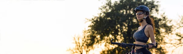 Girl on a mountain bike on offroad, beautiful portrait of a cyclist at sunset, Fitness girl rides a modern carbon fiber mountain bike in sportswear. Close-up portrait of a girl in a helmet and glasses