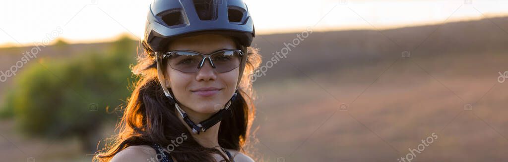 Girl on a mountain bike on offroad, beautiful portrait of a cyclist at sunset, Fitness girl rides a modern carbon fiber mountain bike in sportswear. Close-up portrait of a girl in a helmet and glasses