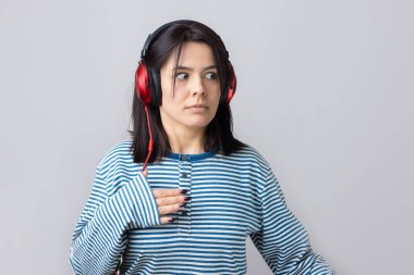 Çizgili yelek giymiş genç bir kız stüdyoda kırmızı kulaklıkla müzik dinliyor ve dans ediyor..