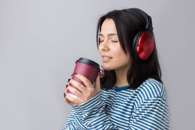 Çizgili yelek giymiş genç bir kız stüdyoda kırmızı kulaklıkla müzik dinliyor ve dans ediyor..