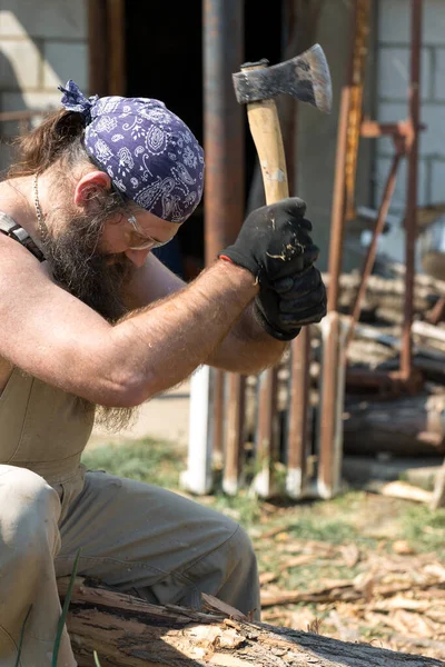 バンダナをした中年の髭の男が斧で丸太を切る 全体的に残酷な暑い日にハードワークを行います — ストック写真