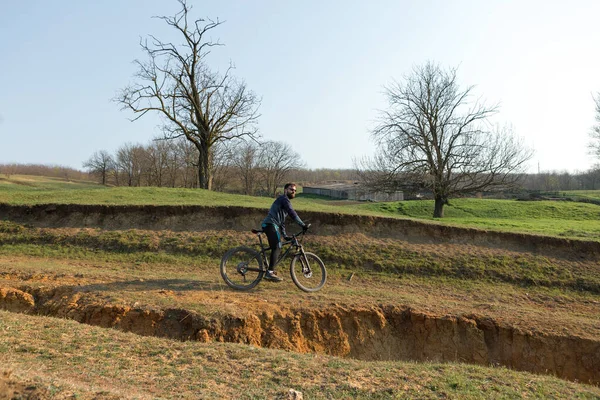 Cyclist in shorts and jersey on a modern carbon hardtail bike with an air suspension fork standing on a cliff against the background of fresh green spring forest