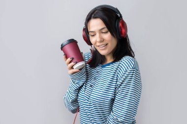 Çizgili yelek giymiş genç bir kız stüdyoda kırmızı kulaklıkla müzik dinliyor ve dans ediyor..