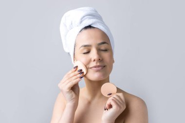 Kafasında beyaz havluyla güzel bir kadın portresi ve pembe bir kalbe bakan bir vücut için sünger. Cilt temizleme eko organik kozmetik rahatlama konsepti.