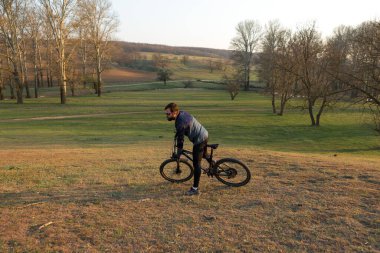 Şortlu ve formalı bisikletçi, modern karbon kuyruklu motorsikletli. Uçurumun kenarında, yeşil bahar ormanlarının arka planında duran bir hava süspansiyon çatalı var.