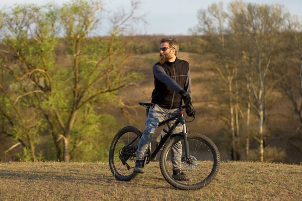 現代のマウンテンバイクで残酷な髭の男をスポーツ 春の緑の丘の上のサイクリスト — ストック写真