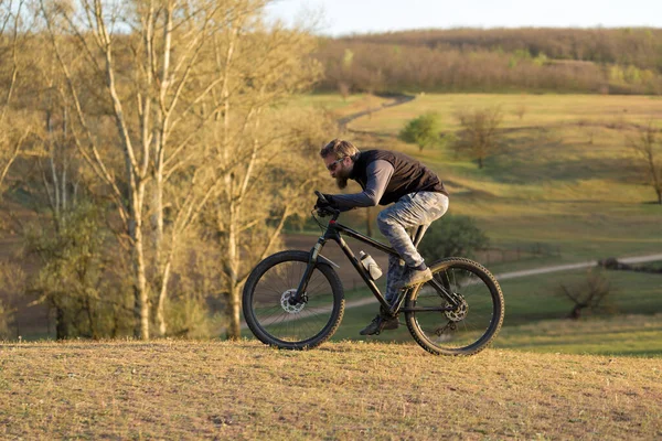 Modern Dağ Bisikletindeki Vahşi Sakallı Adam Baharda Yeşil Tepelerde Bisikletçi — Stok fotoğraf