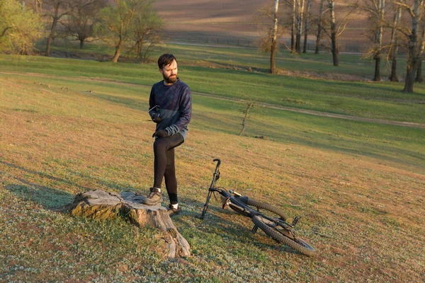 Cyclist in shorts and jersey on a modern carbon hardtail bike with an air suspension fork standing on a cliff against the background of fresh green spring forest