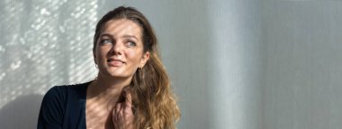 Arka planda, gölgeli gri bir duvarın üzerinde, penceresinden yansıyan doğal ışık olan güzel bir kızın portresi..