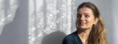 Arka planda, gölgeli gri bir duvarın üzerinde, penceresinden yansıyan doğal ışık olan güzel bir kızın portresi..