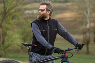 Modern dağ bisikletindeki vahşi sakallı adam. Baharda yeşil tepelerde bisikletçi.