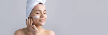 Kafasında beyaz havlu olan bir kadının güzel portresi yüzüne krem sürüyor. Cilt temizleme eko organik kozmetik rahatlama konsepti.
