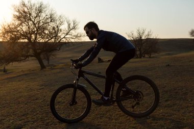 Şortlu ve formalı bisikletçi, modern karbon kuyruklu motorsikletli. Uçurumun kenarında, yeşil bahar ormanlarının arka planında duran bir hava süspansiyon çatalı var.