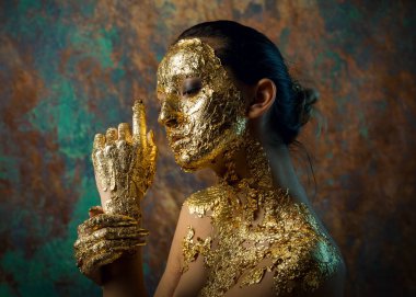 Yüzünde altın yapraktan yapılmış bir maske olan bir kız. Soyut bir arka planda esmer bir kadının kasvetli stüdyo portresi.