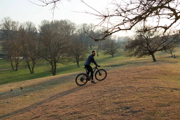 Cyclist in shorts and jersey on a modern carbon hardtail bike with an air suspension fork standing on a cliff against the background of fresh green spring forest