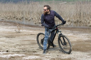 Modern dağ bisikletindeki vahşi sakallı adam. Gölün kenarındaki tuzlu bir yerde bir bisikletçi..